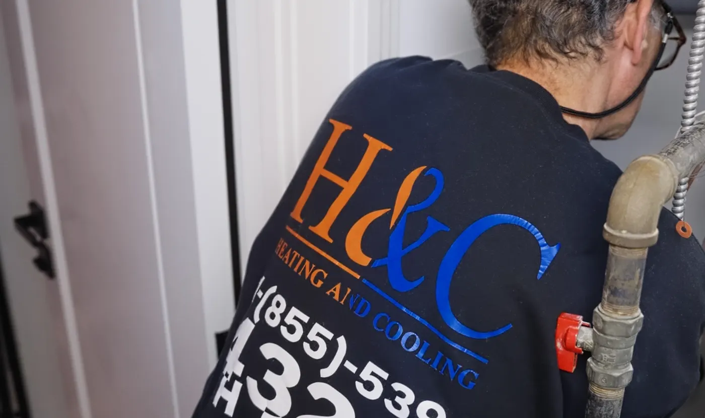 H&C technician working on water lines — crew sweater logo in view
